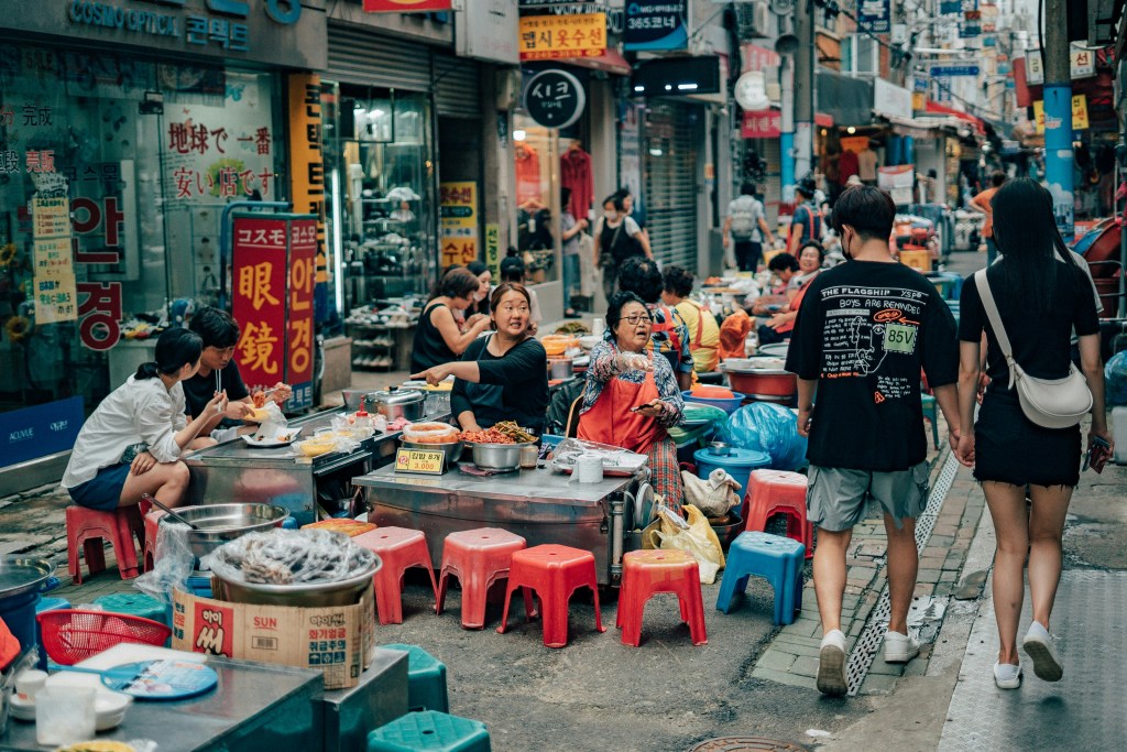A bustling local market near Haeundae Beach with colorful food stalls and people browsing for snacks.