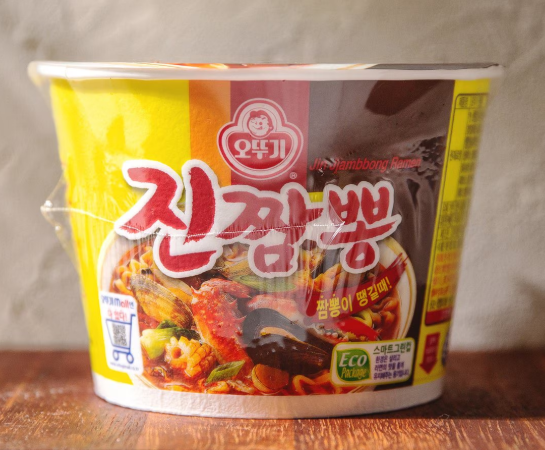A close-up of Jin Jjambbong instant noodles, showcasing a bold red package with spicy seafood flavor branding.