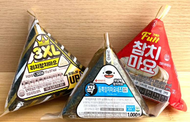 A triangular Korean rice ball (samgak kimbap) wrapped in seaweed, with flavor label such as Tuna Mayo.