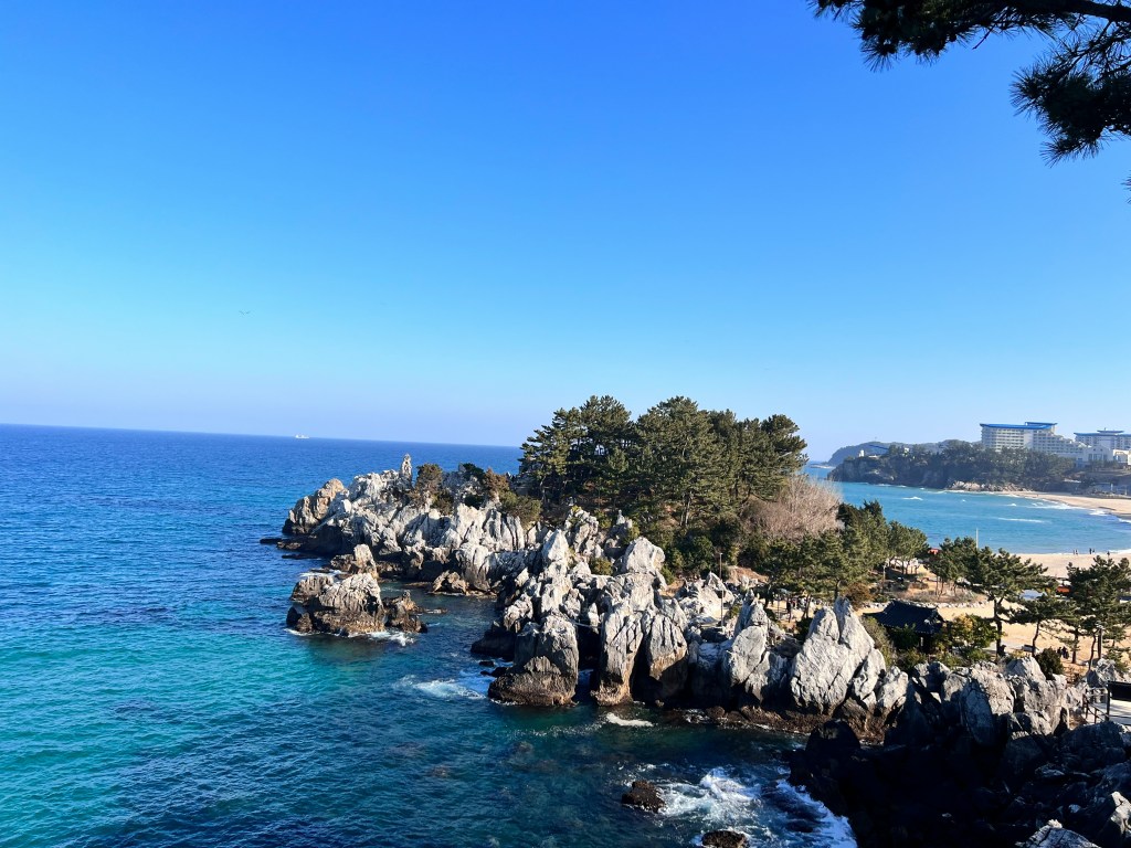 A serene seaside view in Gangneung with a wooden boardwalk, calm sea, and soft clouds overhead.