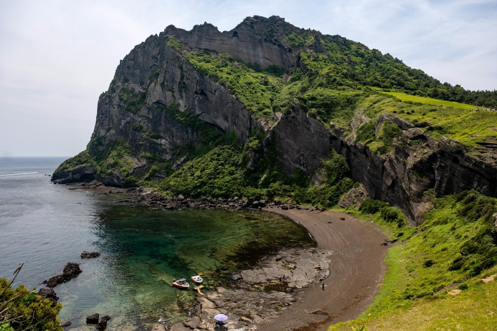 A dramatic coastal cliff on Jeju Island with crashing waves below and volcanic rock formations.