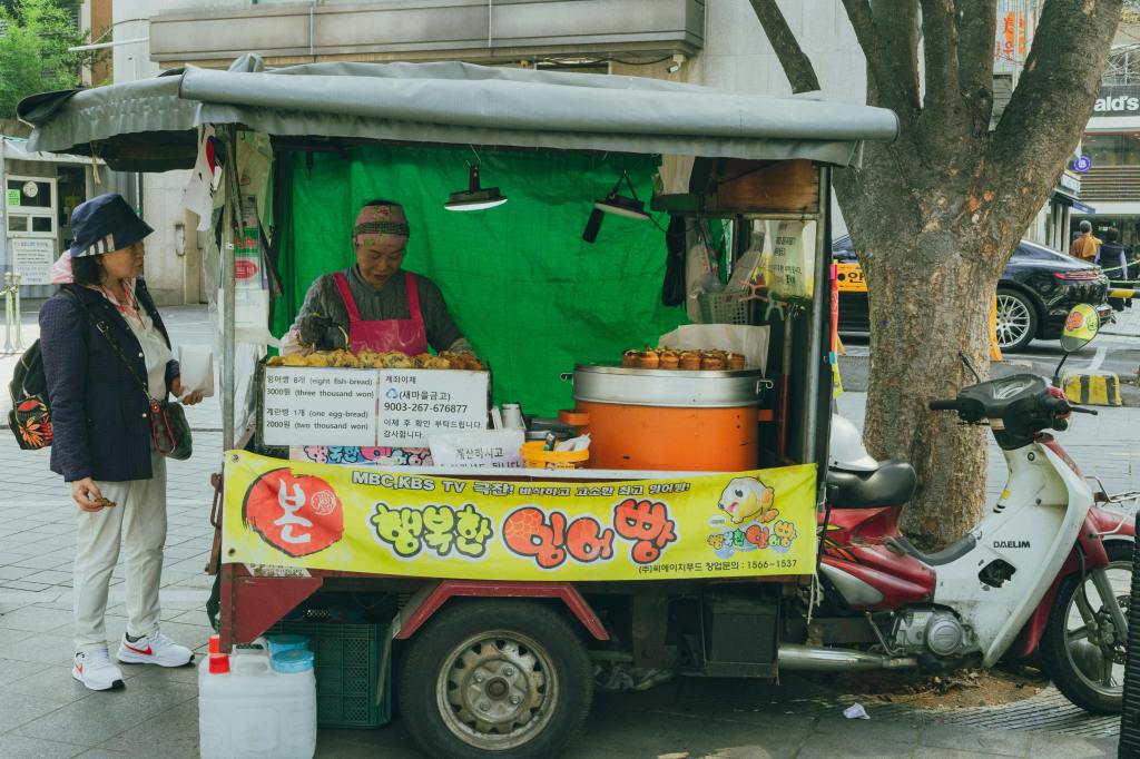 A Korean street food stall selling bungeoppang (fish-shaped pastries), with golden pastries displayed on a griddle.