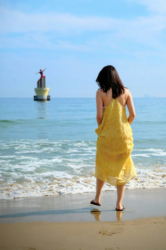 A woman enjoying the ocean breeze at Haeundae Beach, standing on the sand with waves in the background.